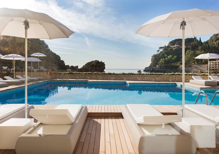 Outdoor pool with large, white umbrellas and white reclining chairs