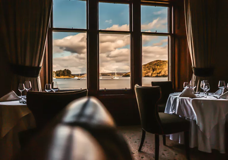 Dining tables with wine glasses and large windows looking out to a lake