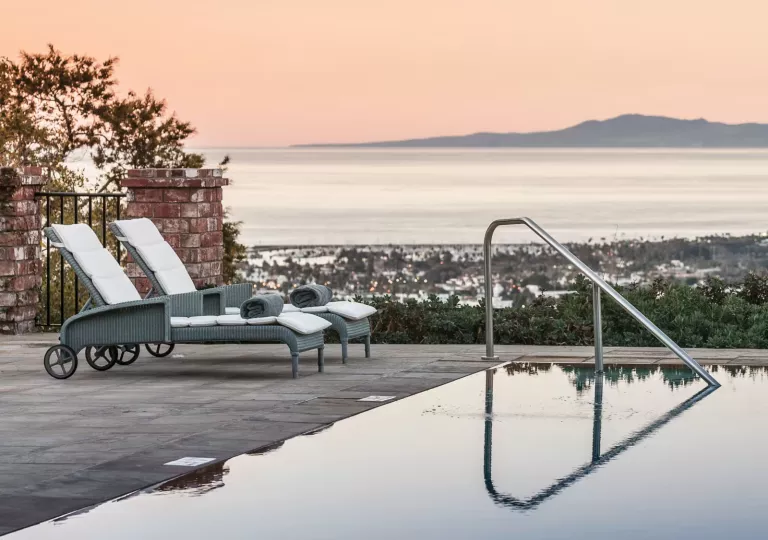 Outdoor pool with two pool chairs, overlooking a town and the ocean