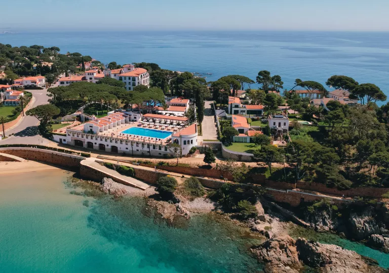 Sky view of buildings surrounded by tees on a cliff next to the ocean