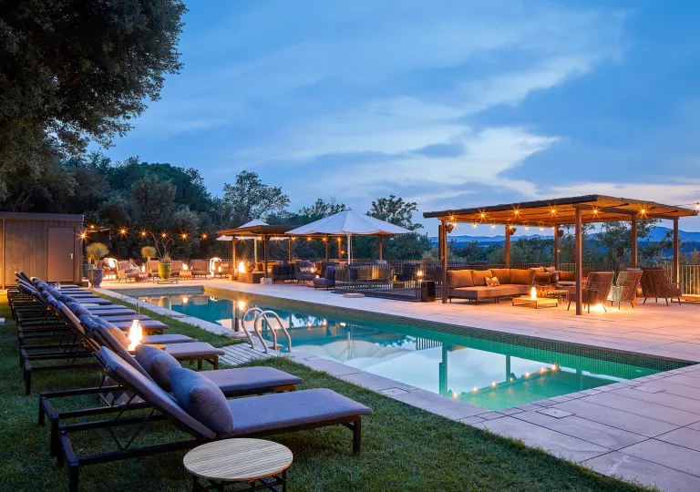 Outdoor pool surrounded by cushioned seats, with canopies with string lights attached