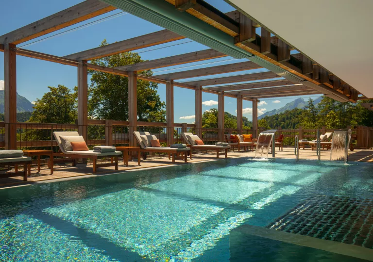 Outdoor pool surrounded by cushioned, reclined chairs and wooden pillars