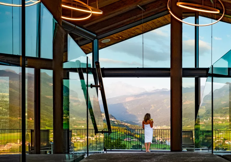 Woman wrapped in a white towel looking at a grassy, mountain
