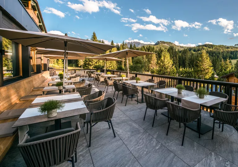 Outdoor dining area with woven, brown chairs, looking out to a valley of trees