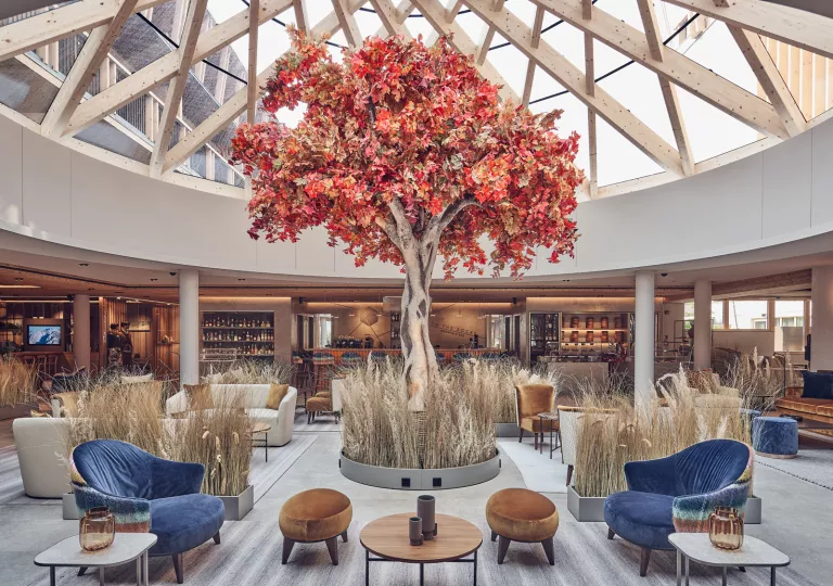 Large, indoor lobby with a glass ceiling and a large red tree in the middle