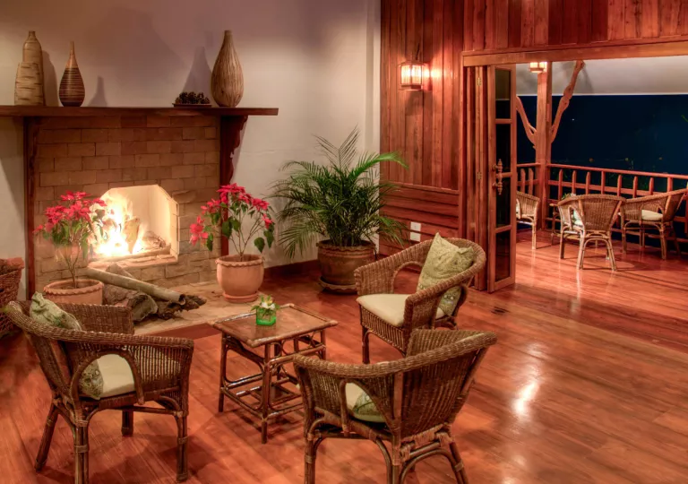 Indoor cabin room with a fireplace and woven chairs, with a patio to the right