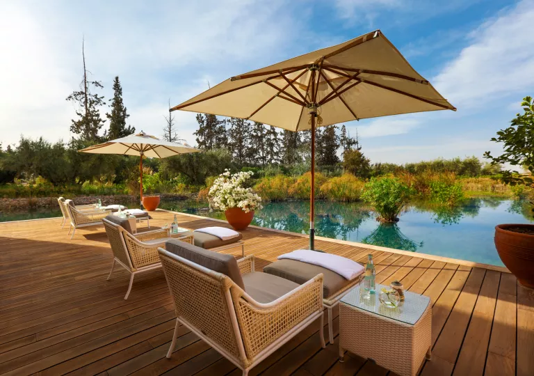 Woven, outdoor pool chairs surrounding a lake, on a wooden balcony