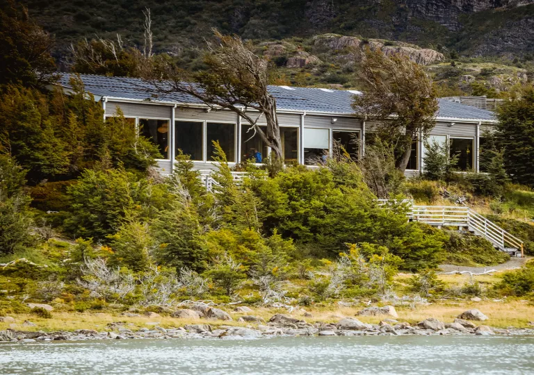 Building with wide windows, surrounded by trees next to a lake