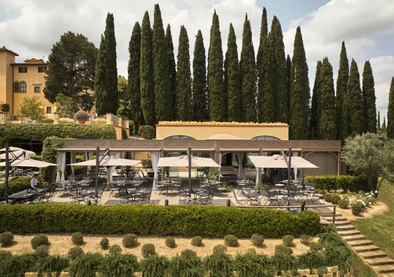Outdoor garden and patio, with trimmed bushes and black chairs and tables