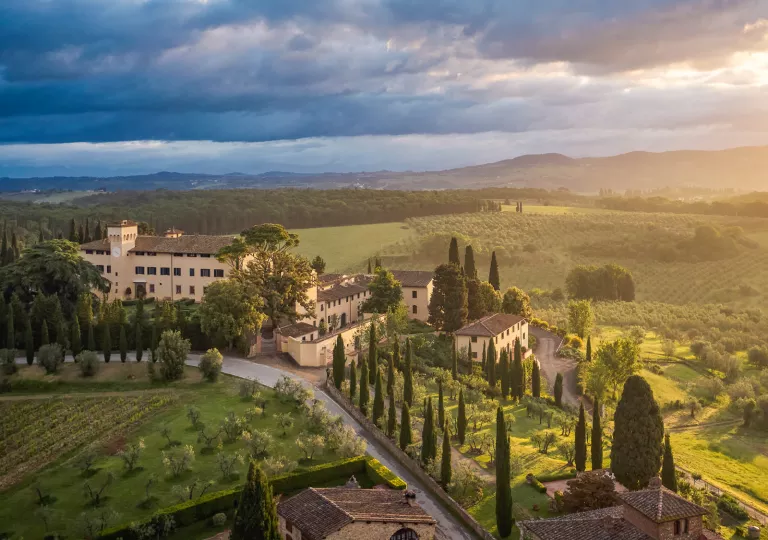 Exterior view of tan and brown buildings, surrounded by large crop fields and mountains