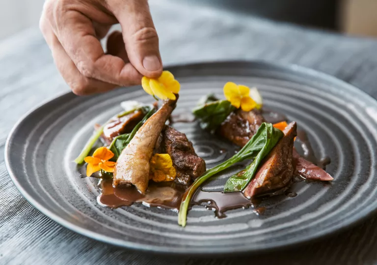 Black, ribbed plate with meat in a brown sauce, decorated with flowers