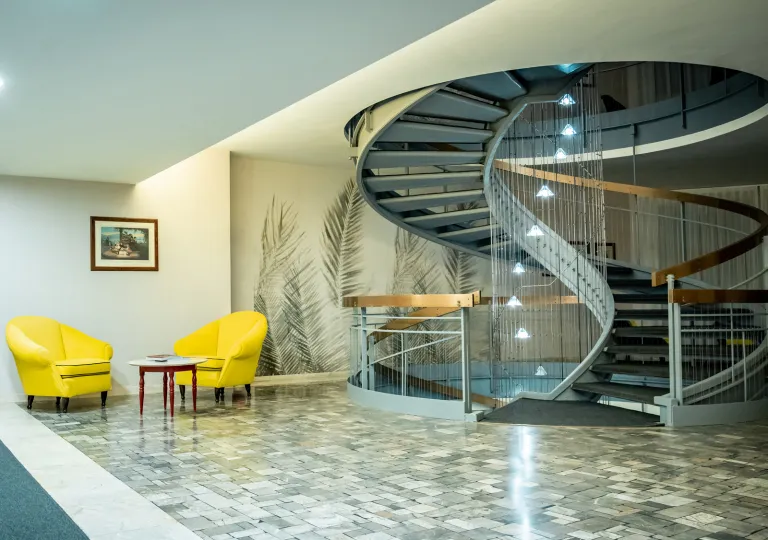Room with a gray, spiral staircase with two yellow chairs on the left