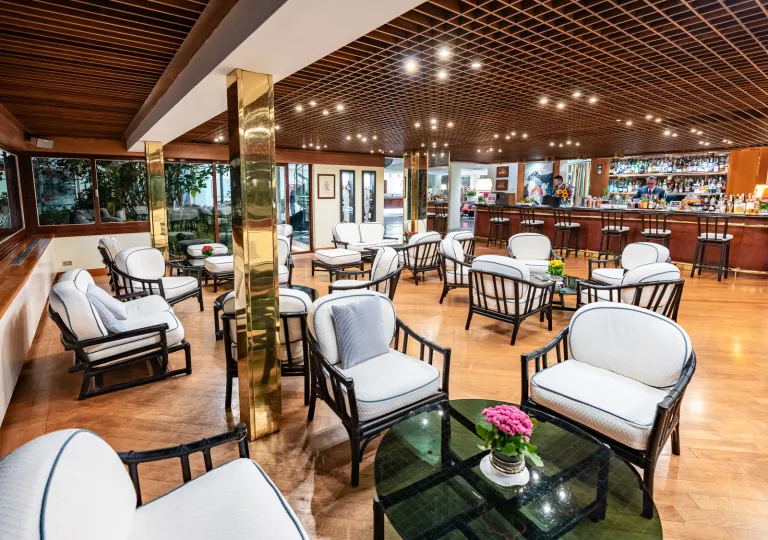 Bar and lounge with white, cushioned chairs and circular glass tables
