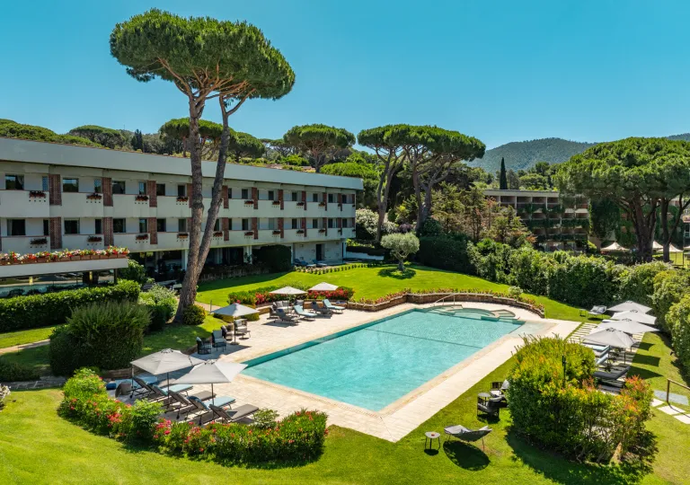 Outdoor pool surrounded by plants and bushes, next to a hotel building