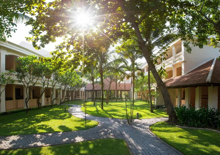 Outdoor courtyard between two white buildings, with a grass field and small palm trees