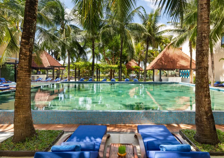 Outdoor pool with small huts and blue, reclining chairs surrounding the pool