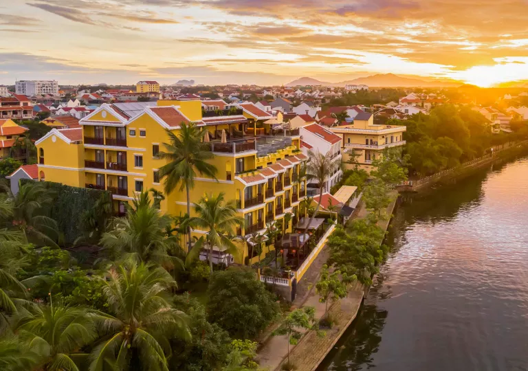 Sky view of yellow hotel building with a lake to the right and the sunset in the background