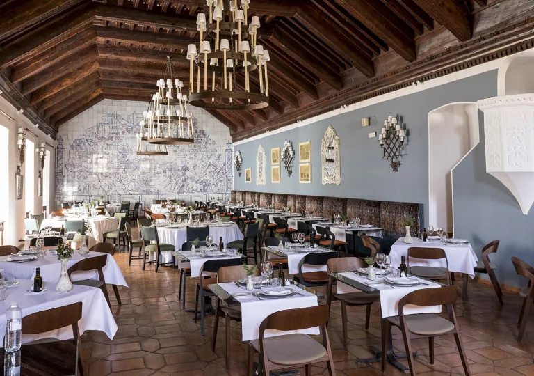 Large dining hall with tables and wooden chairs, with three large candle chandeliers