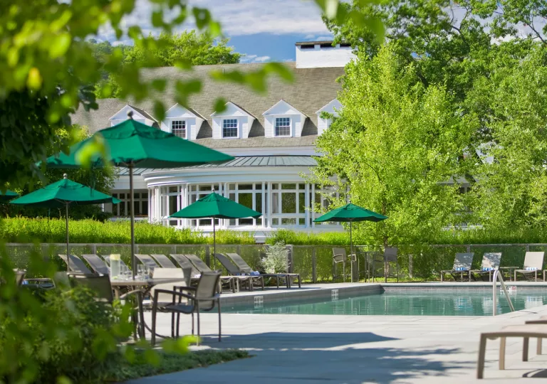 Exterior view of white building with an outdoor pool, surrounded by green umbrellas