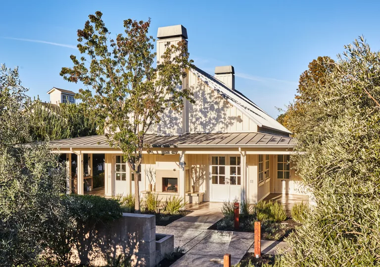 White building with a porch, surrounded by tall trees