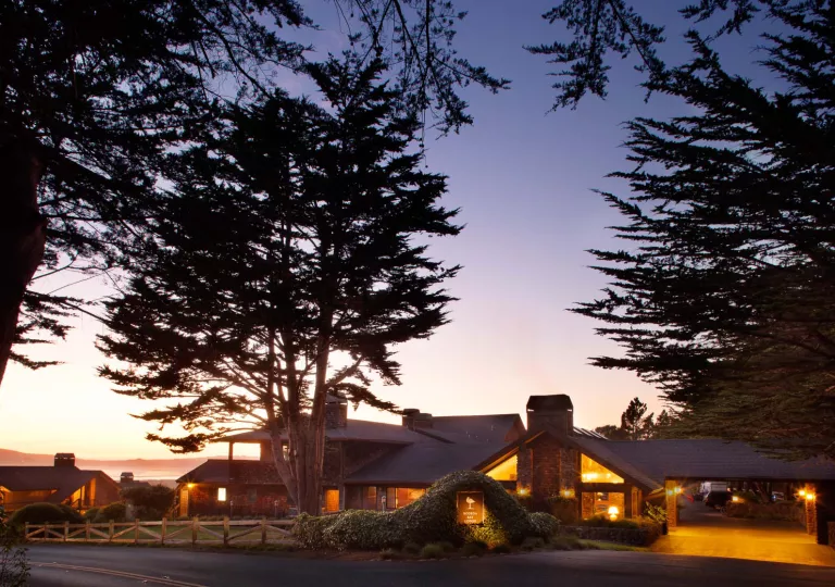 Outdoor view of a hotel entrance, illuminated by orange lights and the sunset