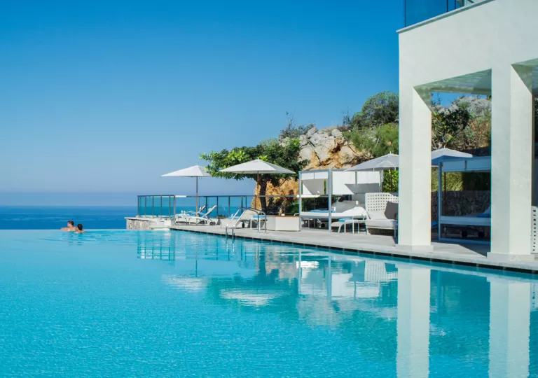 Outdoor infinity pool with a man and woman swimming on the edge, looking out to the ocean