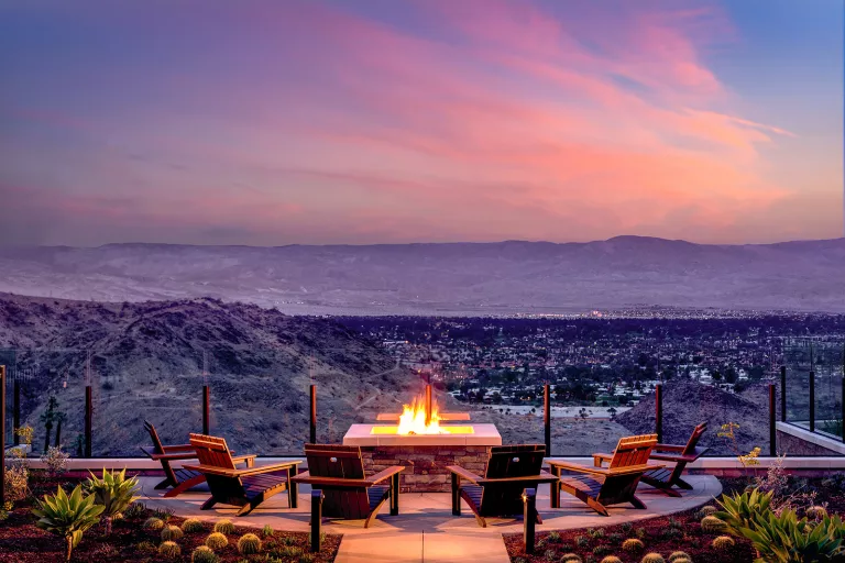 Stone, outdoor patio with a fireplace, looking out to mountains and a large city