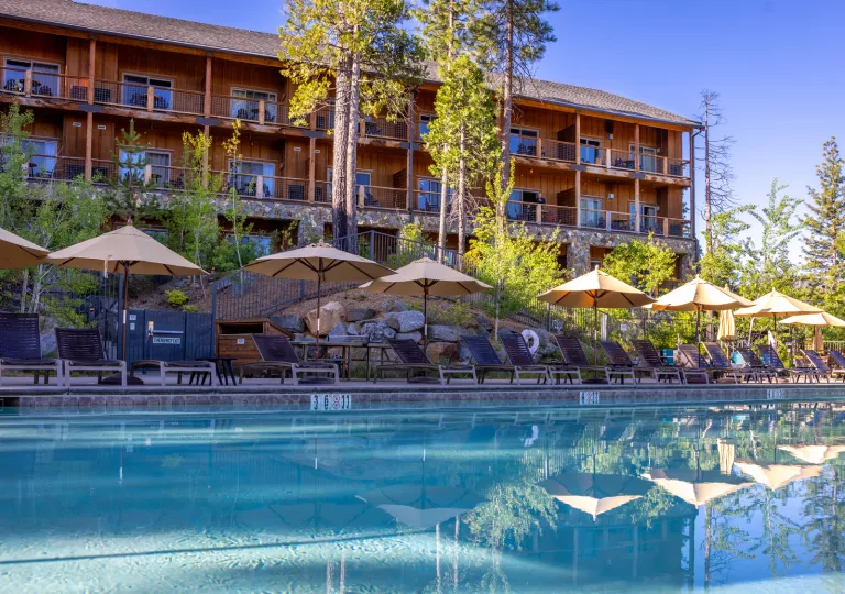 Outdoor pool surrounded by tan umbrellas and a wooden cabin in the background