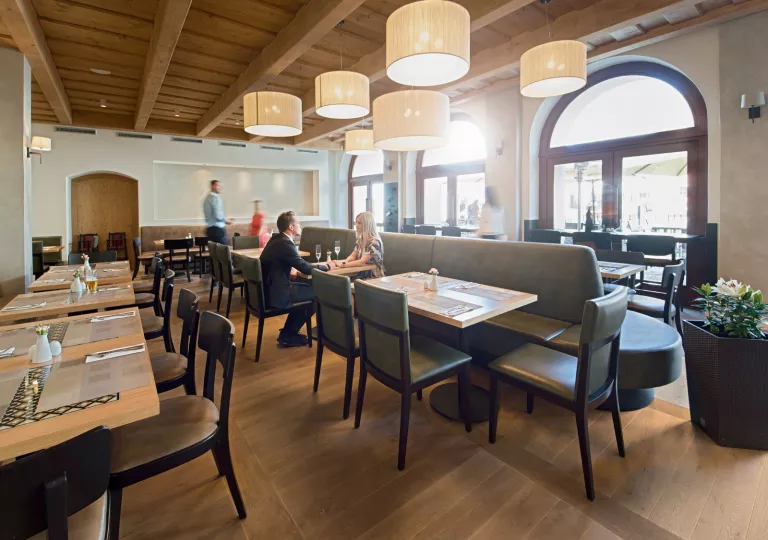 Man and woman sitting in an empty dining hall, with green cushioned chairs and wooden tables