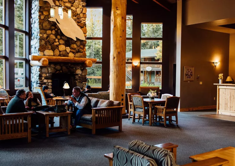 Cabin lobby with large wooden pillars and people sitting in front of a stone fireplace