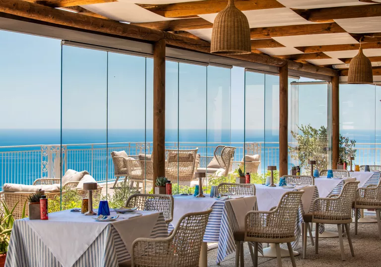 Indoor dining area with large, glass walls looking out to a balcony by the beach
