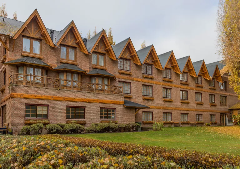 Exterior view of brick hotel building with a grass field and yellow trees in front