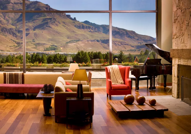 Indoor lobby with cushioned chairs, with large windows looking out to tall hills