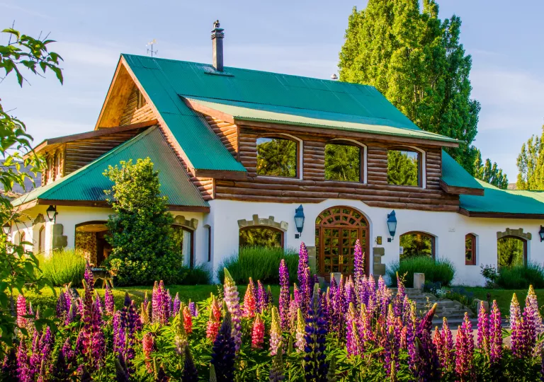 Cabin-style house with a green roof and pink flowers in front