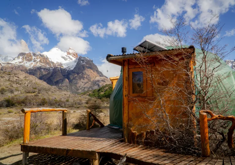 Small wooden hut in the middle of a valley, with large mountains in the distance