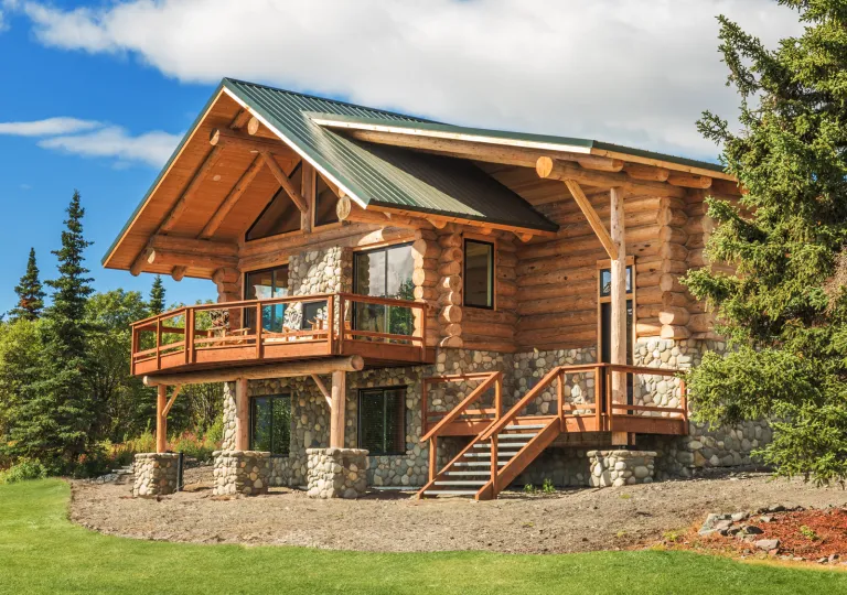 Exterior view of large wooden and stone cabin with trees surrounding