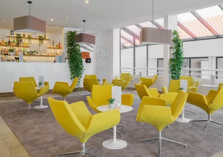 Indoor bar and lounge with yellow chairs and circular, white tables