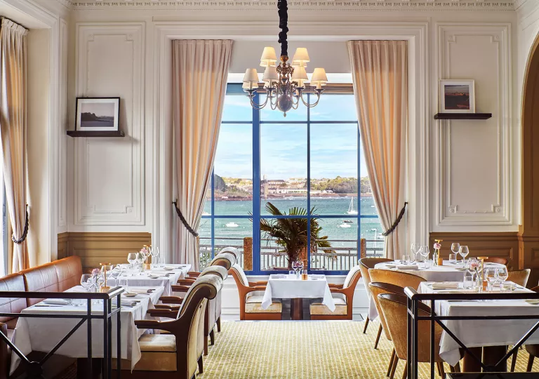Restaurant dining hall with white chairs and tables, with large windows looking out to the ocean