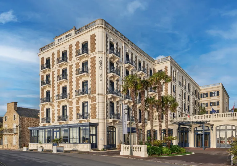 Exterior view of multi-story beige hotel building with palm trees in front