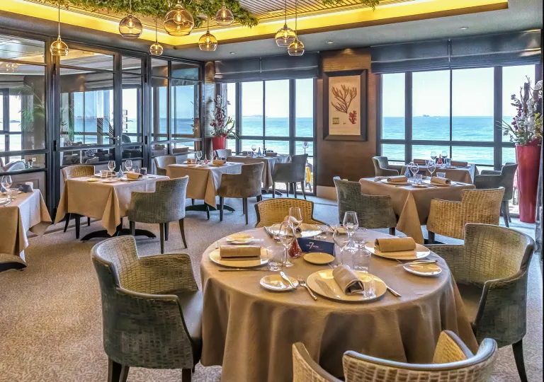 Restaurant with circular tables and large windows with views of the ocean