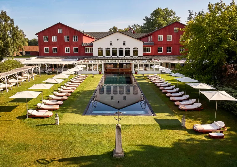 Red and white building with an outdoor pool in front, surrounded by reclining white chairs and white umbrellas