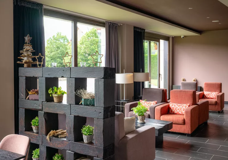 Indoor hotel reception area with cushioned chairs and plants scattered around the room
