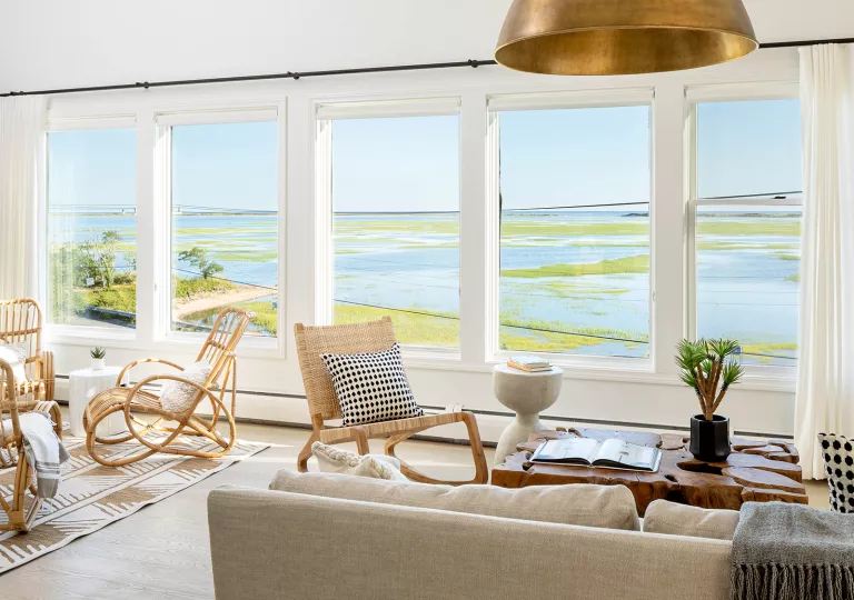 White room with wooden furniture and large windows looking out to a marsh