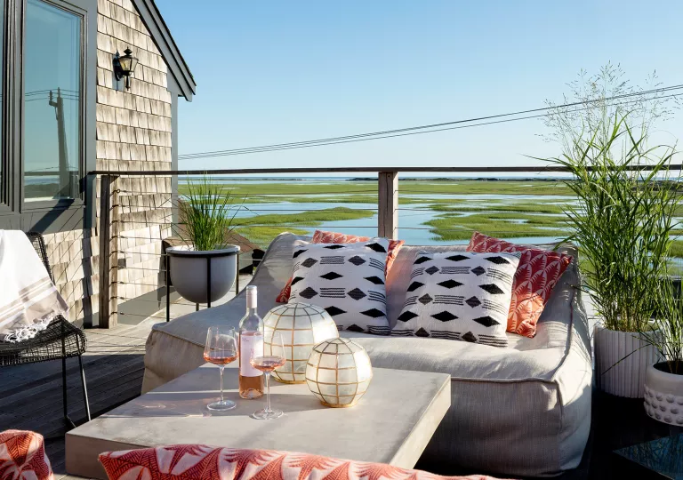 Outdoor balcony with cushioned sofas looking out towards a marsh
