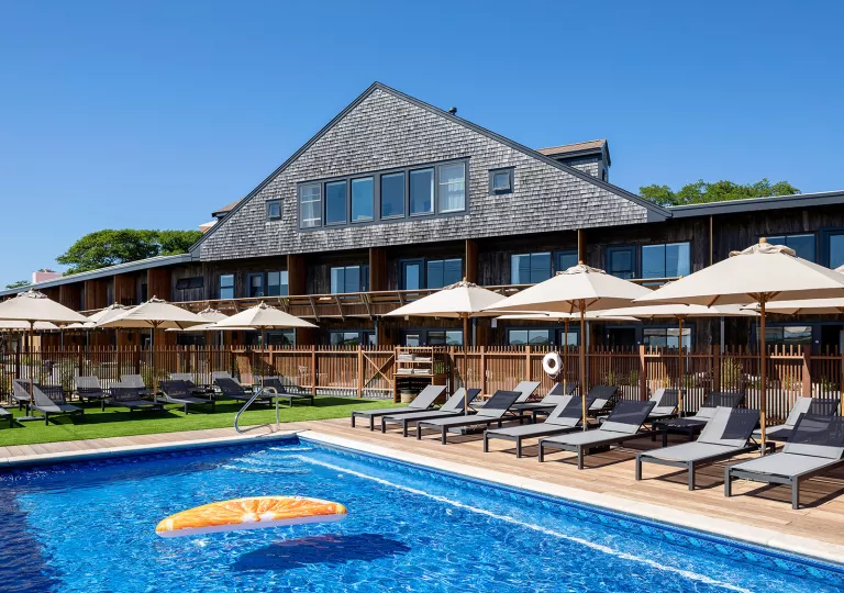 Outdoor pool surrounded by gray chairs and white umbrellas, with a building in the background