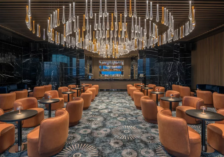 Bar and lounge with orange, cushioned chairs and a large chandelier hanging from the ceiling