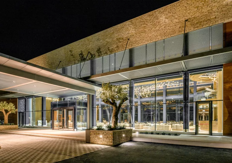 Exterior view of stone hotel building with large windows and trimmed trees in front