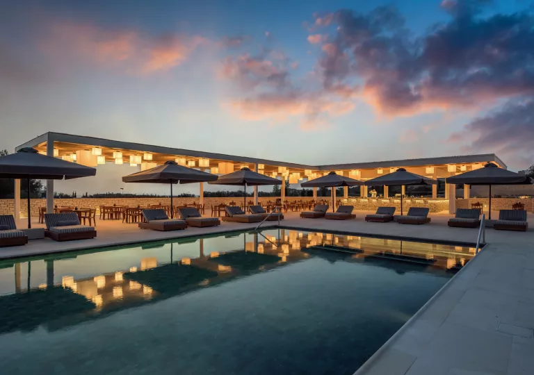 Outdoor pool surrounded by reclining chairs and umbrellas, with light fixtures hanging