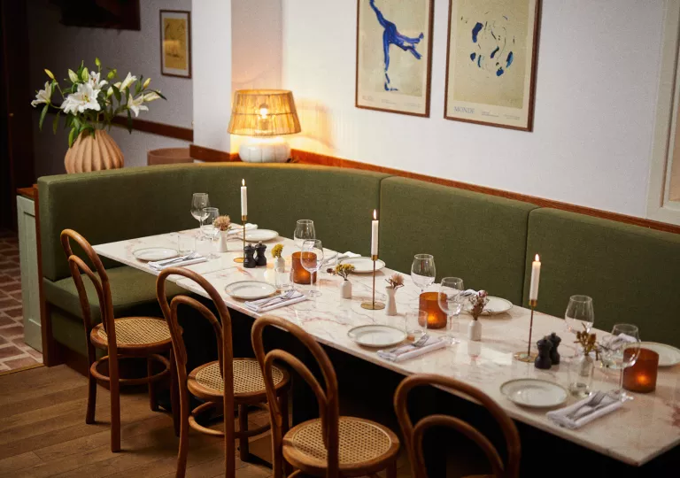 Long dining table with green couches and wooden chairs, with paintings on the walls