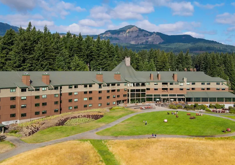 Exterior view of large brown hotel building, with a grass field in front